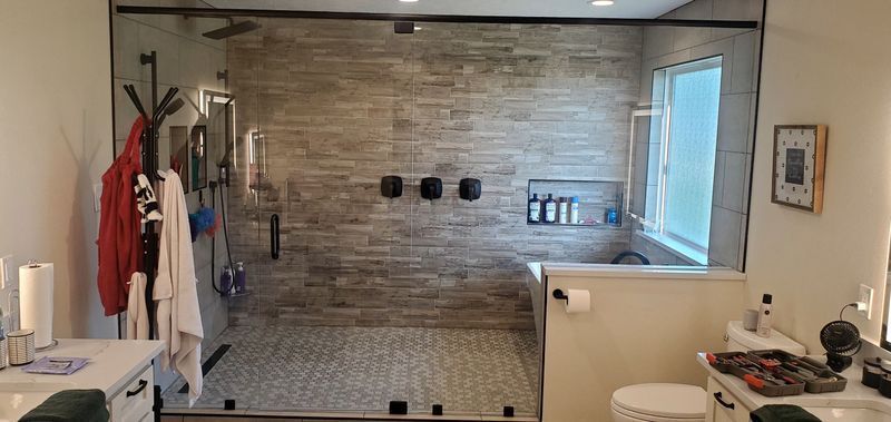 Bathroom with a stone accent shower wall, towels on hooks, and a sink with toiletries beside a window