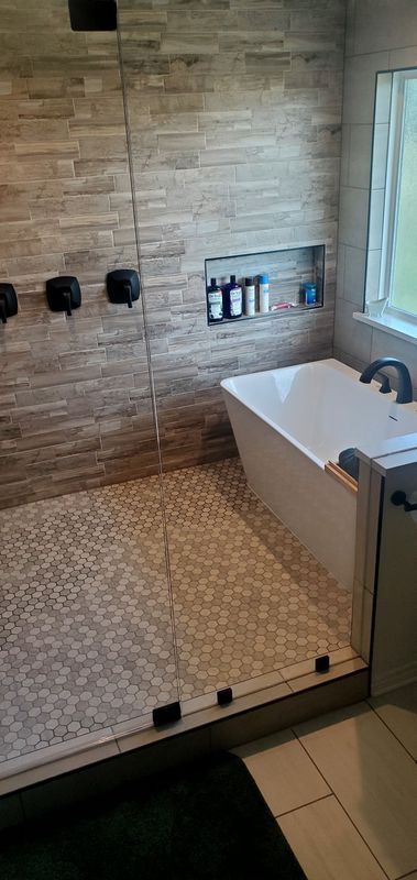 Modern bathroom with walk-in shower, stone-tile walls, pebble floor, and freestanding tub by a window