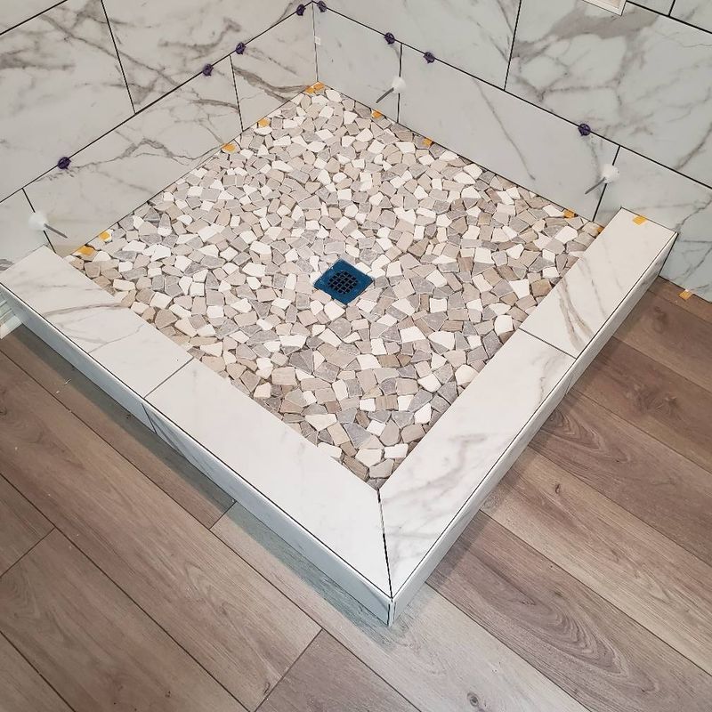 Square tiled shower floor with a blue drain and white marble trim, viewed from above