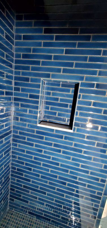 Blue tiled wall with a small black-framed recessed opening and a shower head below