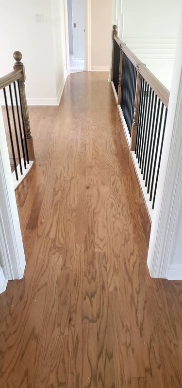 Wooden hallway with white walls and black railing, viewed from the top of stairs