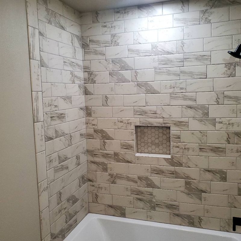 Tiled shower wall with a small recessed niche and white bathtub edge below
