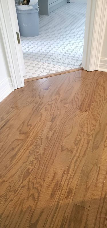 Wooden floor leading into a tiled hallway with a doorway at right