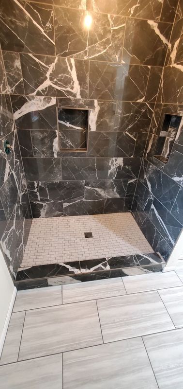 Modern shower with dark stone tile walls, white floor tile, and built-in niches and bench