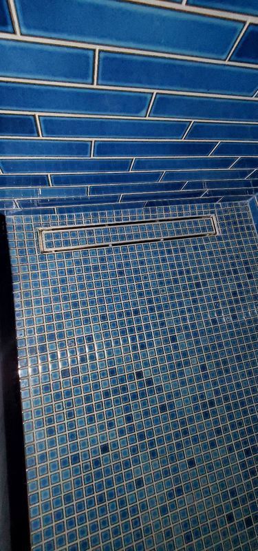 Blue tiled shower wall with a metal drain on the floor
