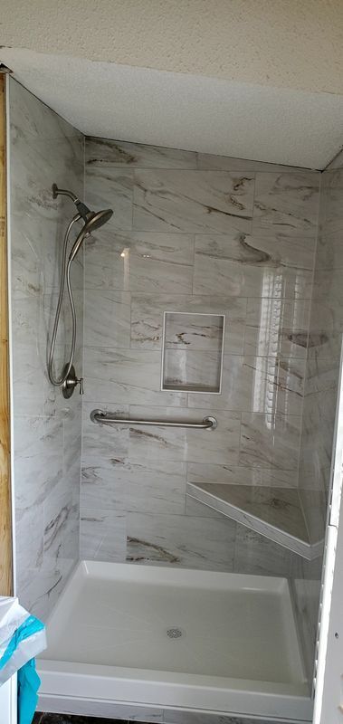Small tiled bathroom shower with white tub, wall-mounted showerhead, and marble-look walls