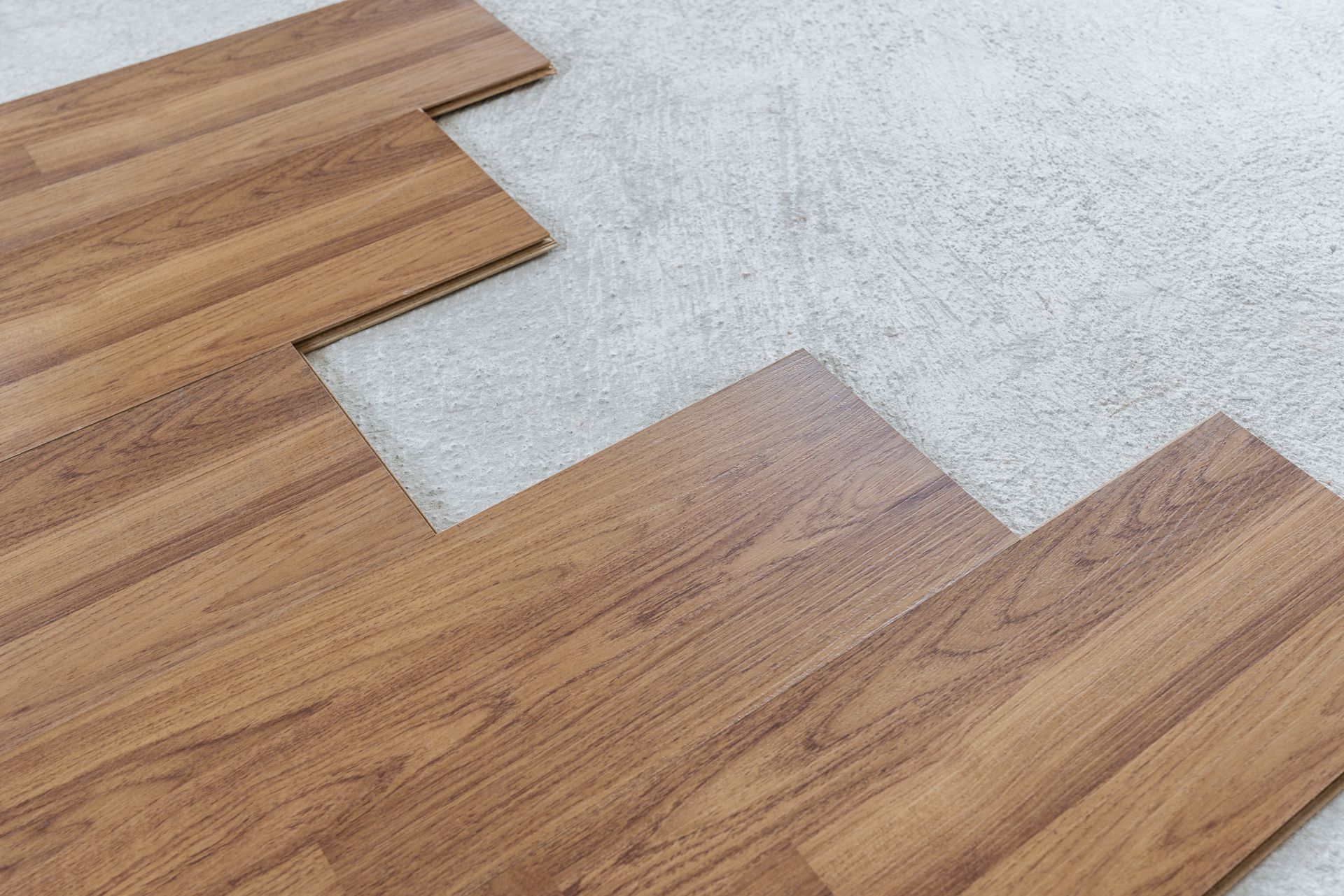 Wooden flooring planks being laid over gray underlayment, with an unfinished edge visible.