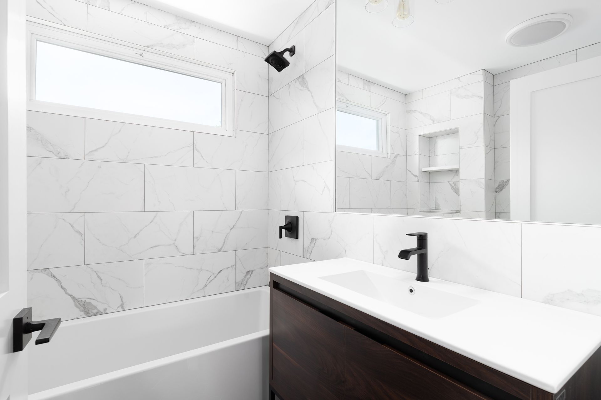 Bright modern bathroom with white tile, black fixtures, bathtub, and vanity mirror