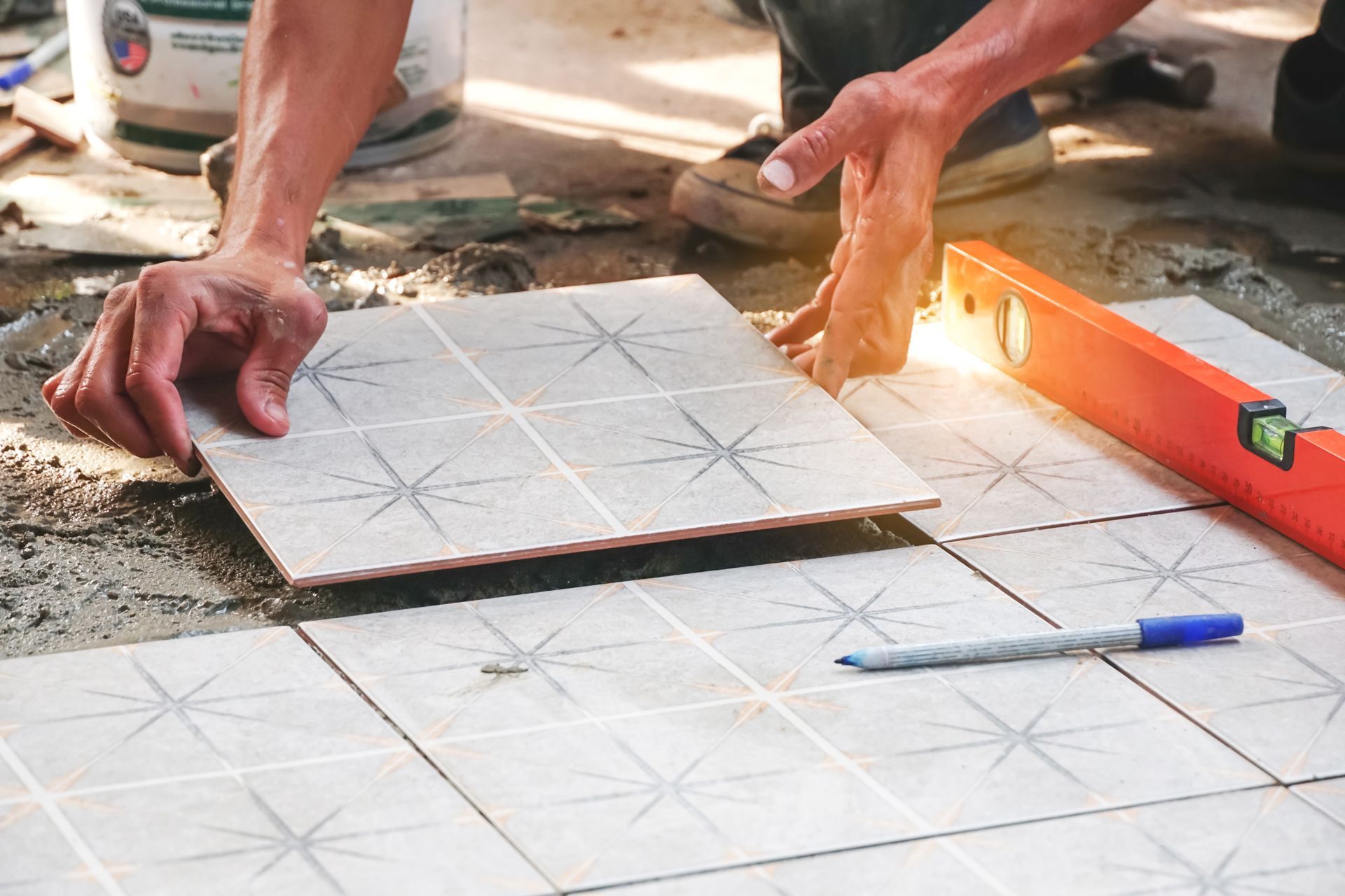 Hands laying white patterned floor tiles with a trowel and level during installation.
