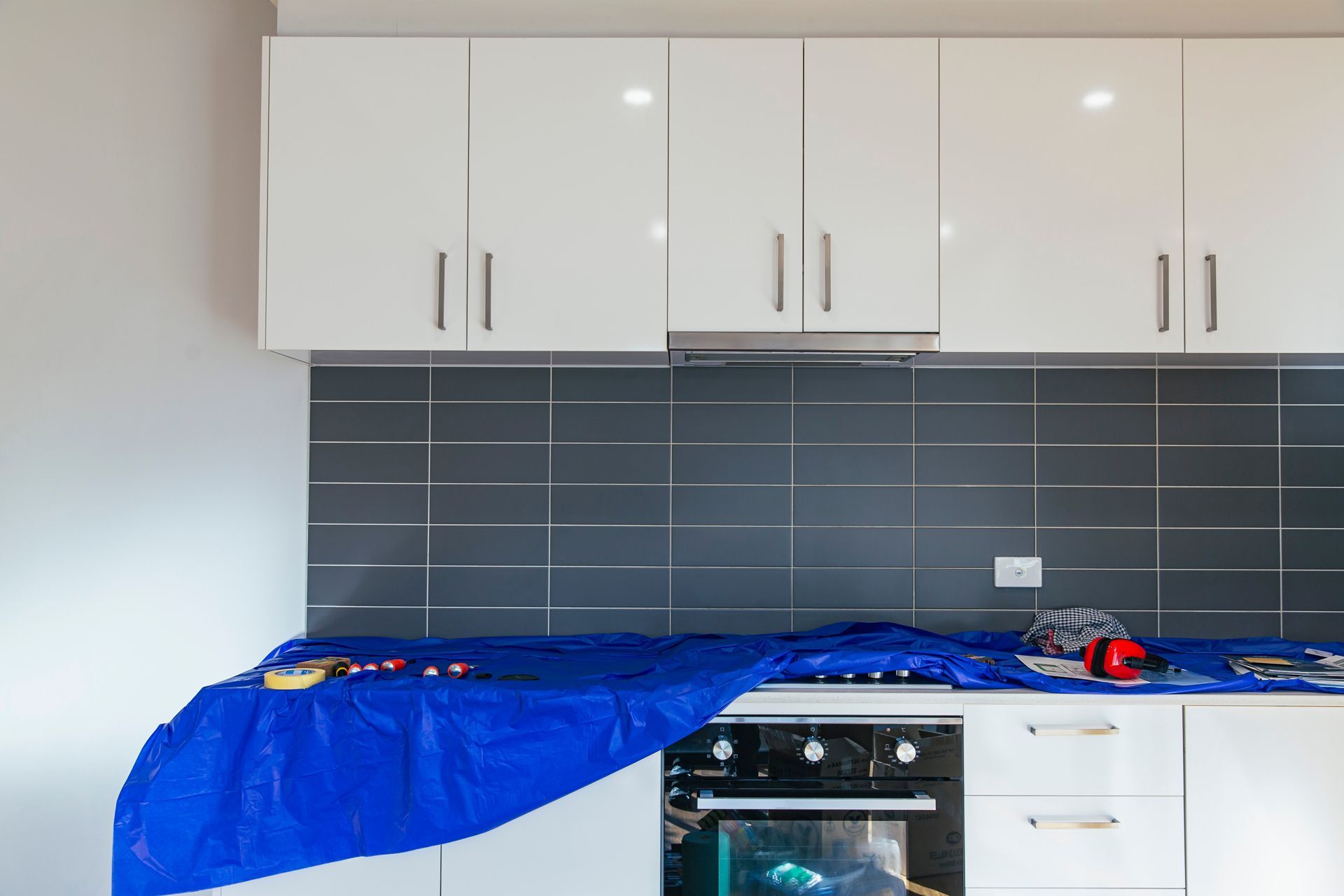 Kitchen with white cabinets, dark tile backsplash, and a blue tarp covering the countertop and stove during renovation