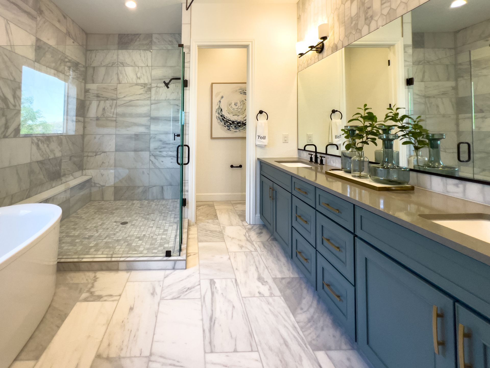 Modern bathroom with marble tile, glass shower, blue vanity, and large mirror
