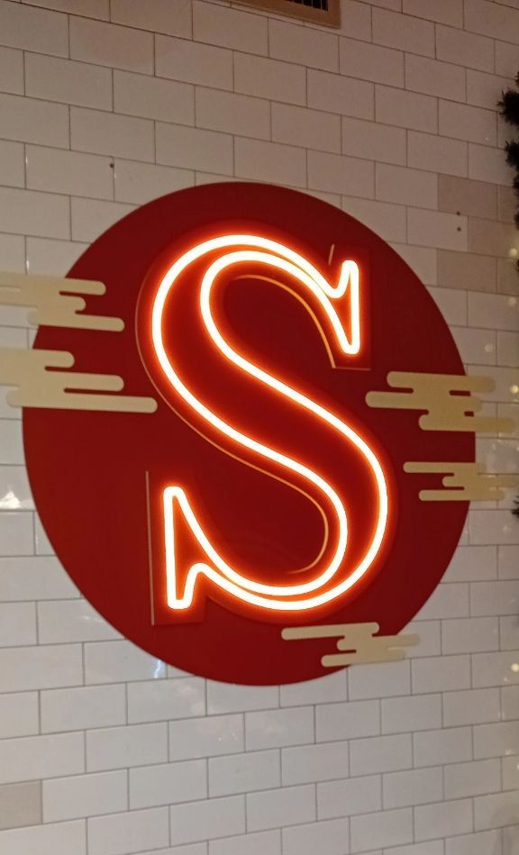 Lettera “S” al neon rossa all'interno di un cerchio rosso su una parete piastrellata di bianco.