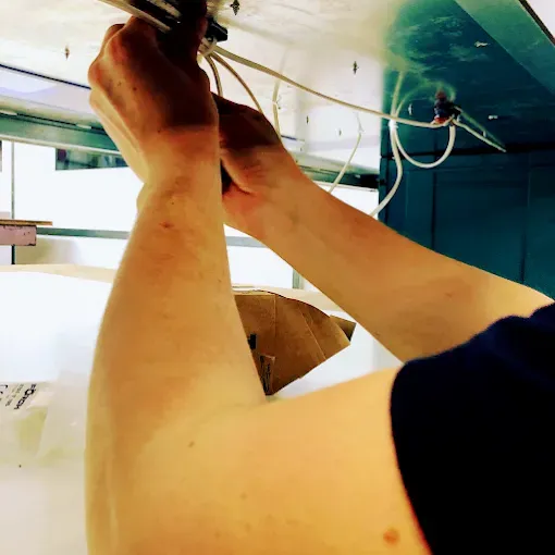 Mani che regolano i cavi sotto un apparecchio a soffitto in uno spazio simile a un'officina.