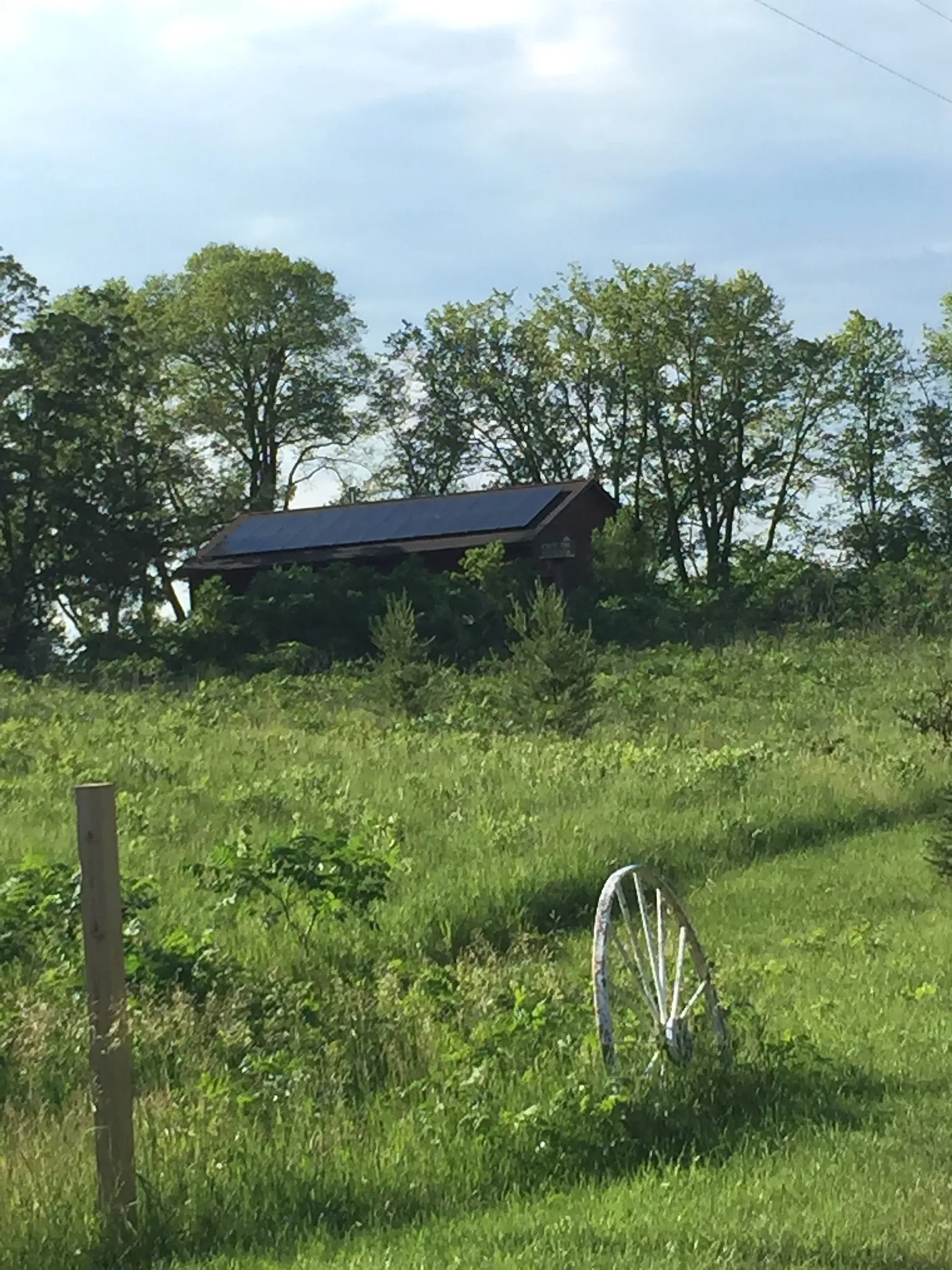 A barn with solar panels on the roof is in the middle of a grassy field.