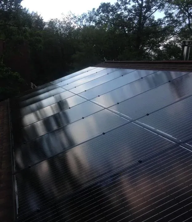 A row of solar panels on a roof with trees in the background