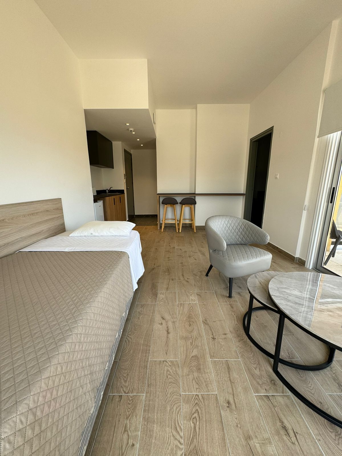 A bright one bedroom apartment featuring an armchair, and coffee table. The open layout leads to a hallway.