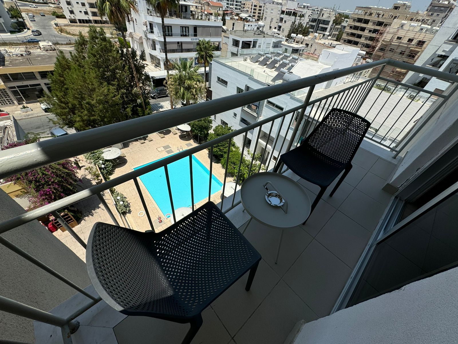 A balcony with two chairs and a table overlooking a swimming pool.