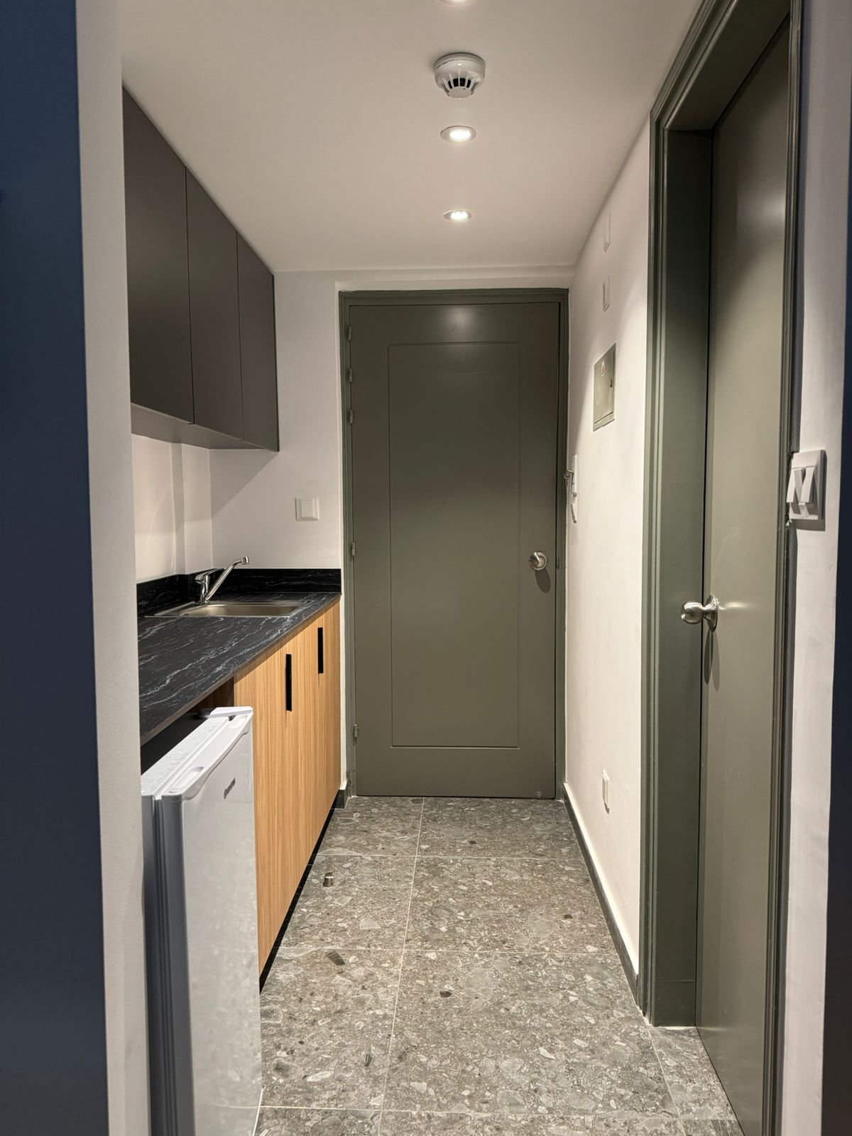 A kitchen with a sink , refrigerator , cabinets and a door.