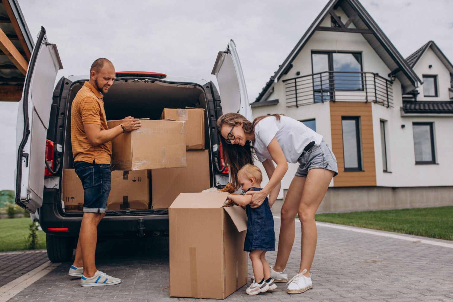 Family unloading moving boxes from a van in front of their new house.
