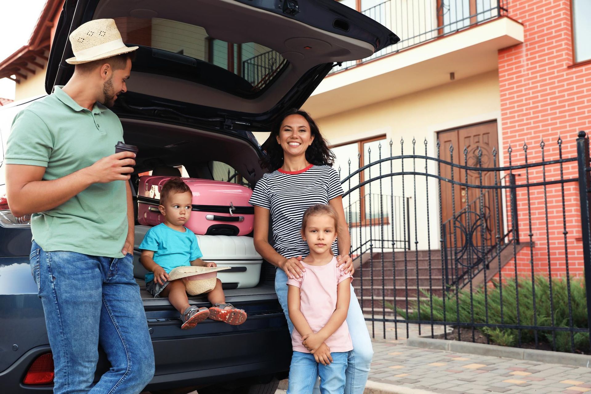 Family sitting in open car trunk in a field. Smiling adults, holding children. Sunlit, warm tones.