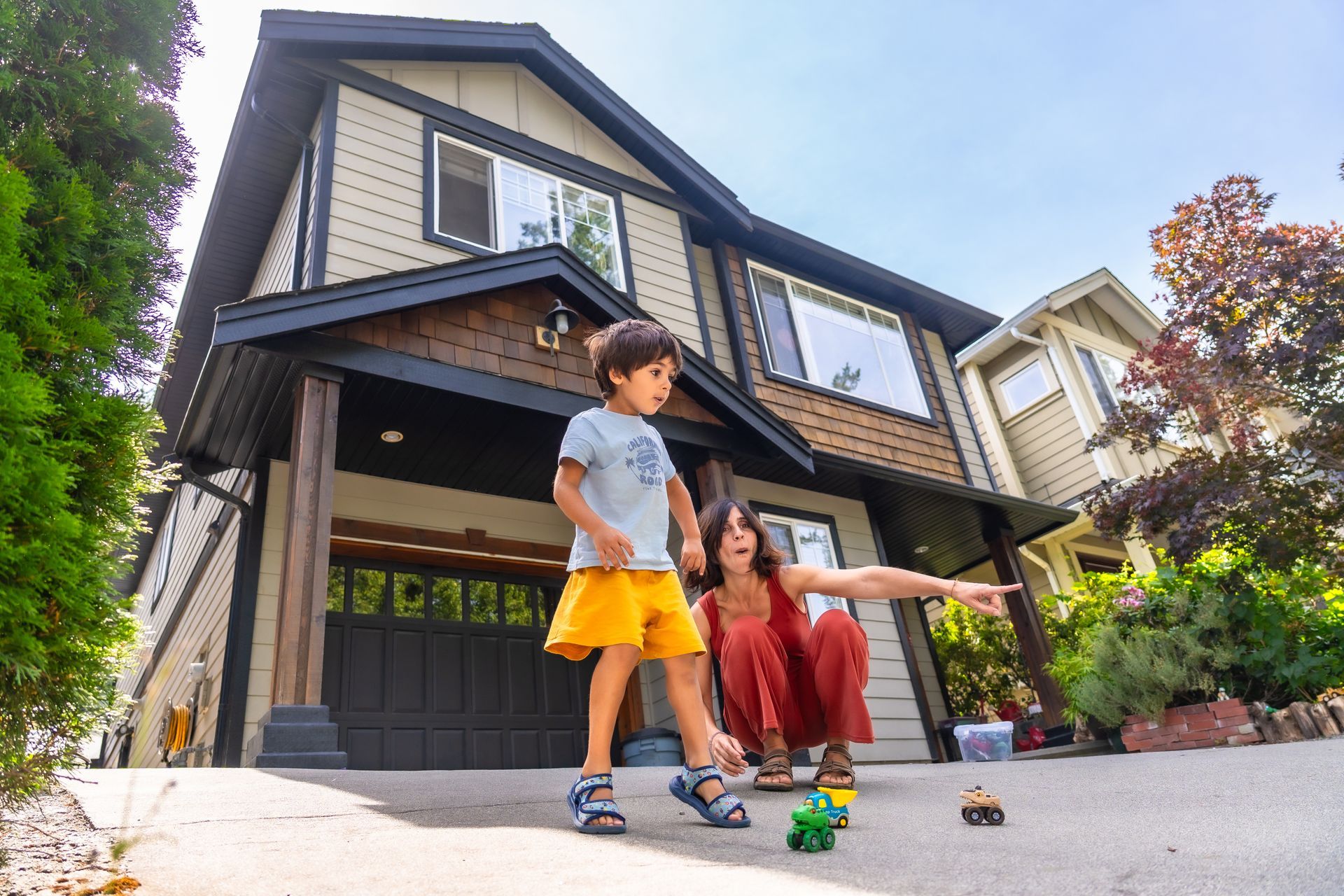 Family with child on shoulders stands by electric car in front of building.