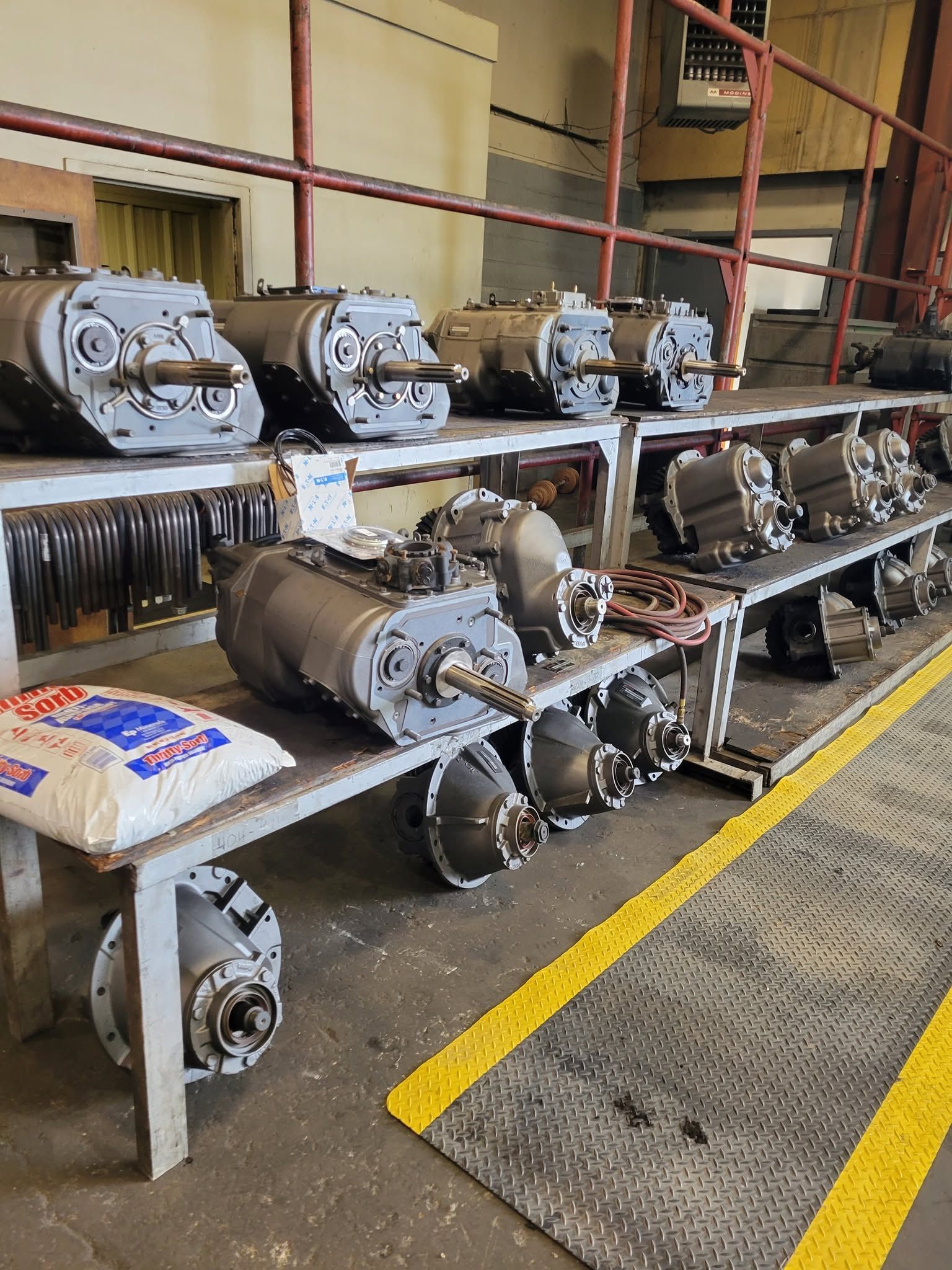 Row of metal engines and parts on shelves in an industrial workshop, with a yellow floor line