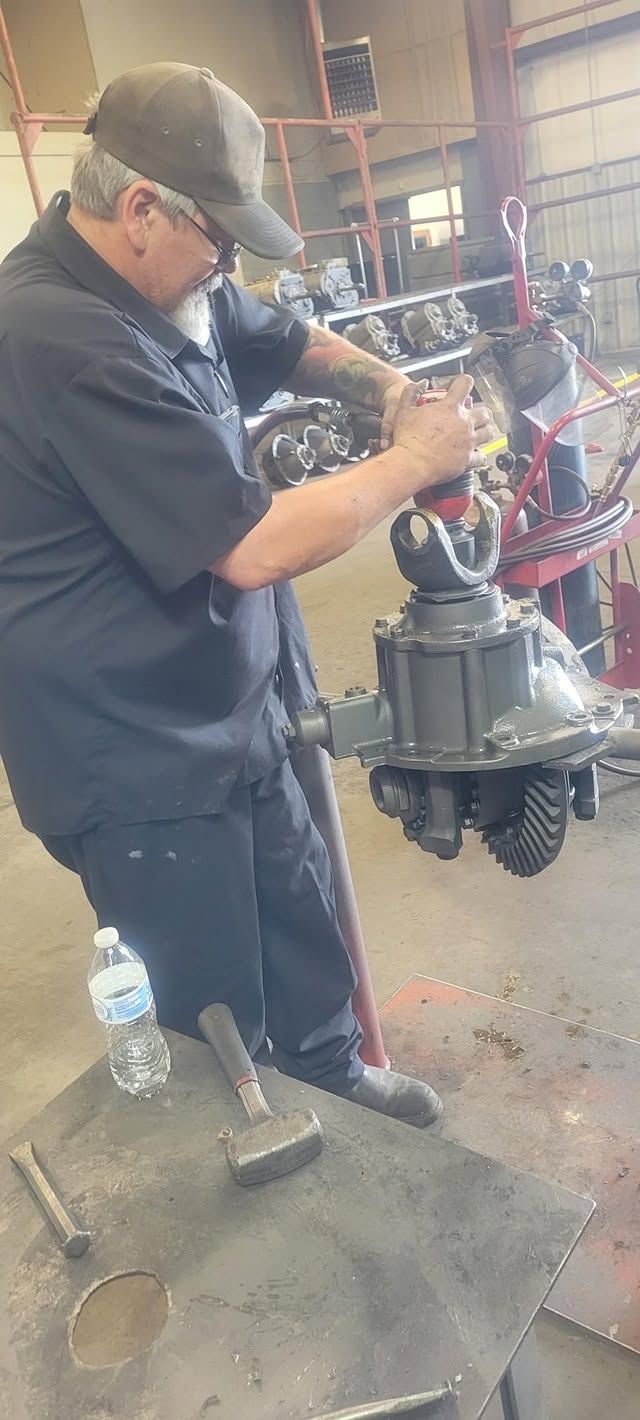 Mechanic in dark uniform working on a large machine in a workshop, with tools and parts nearby