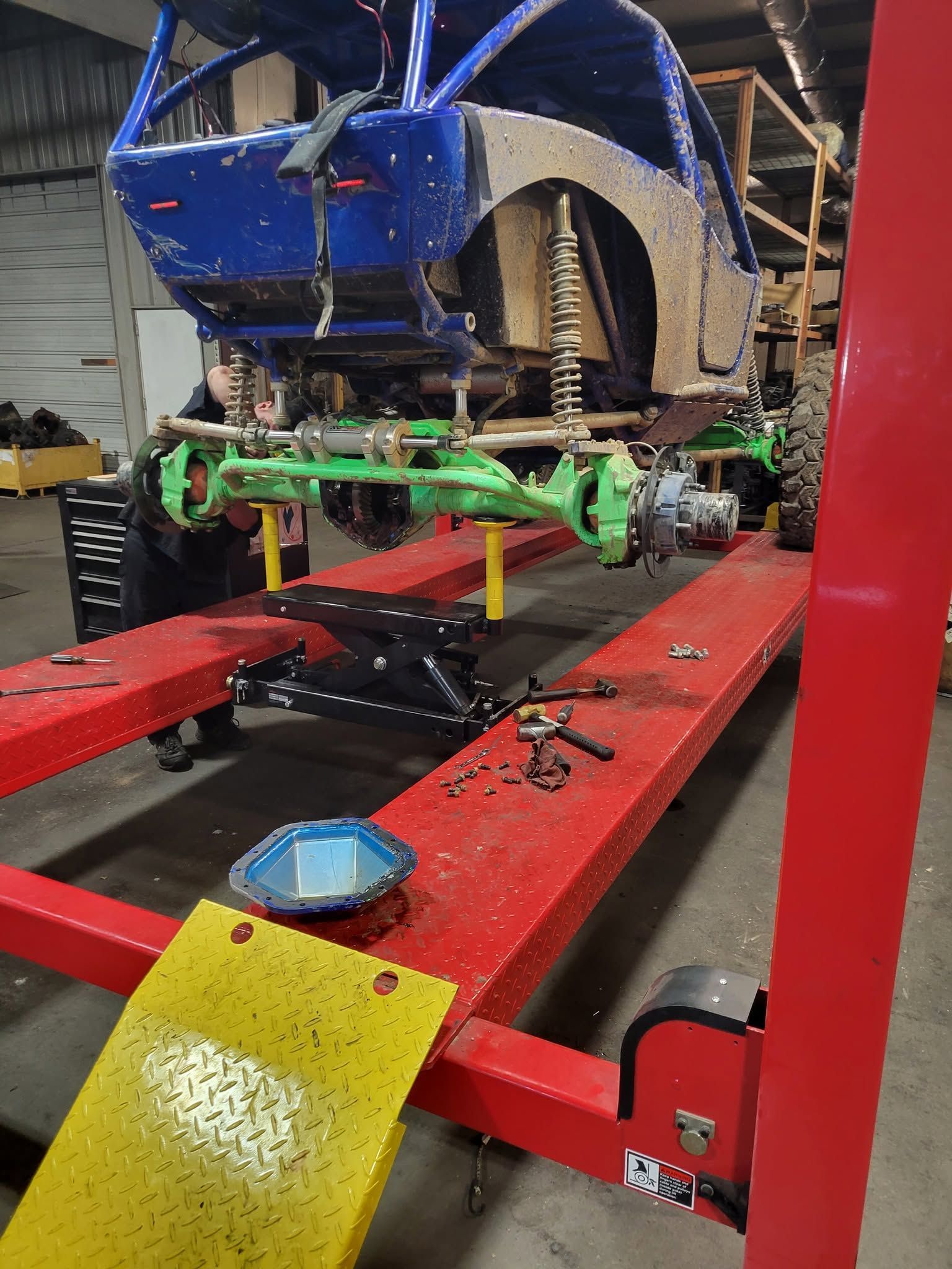 Blue car on a red alignment rack in an auto shop, with exposed suspension and wheel hub removed.
