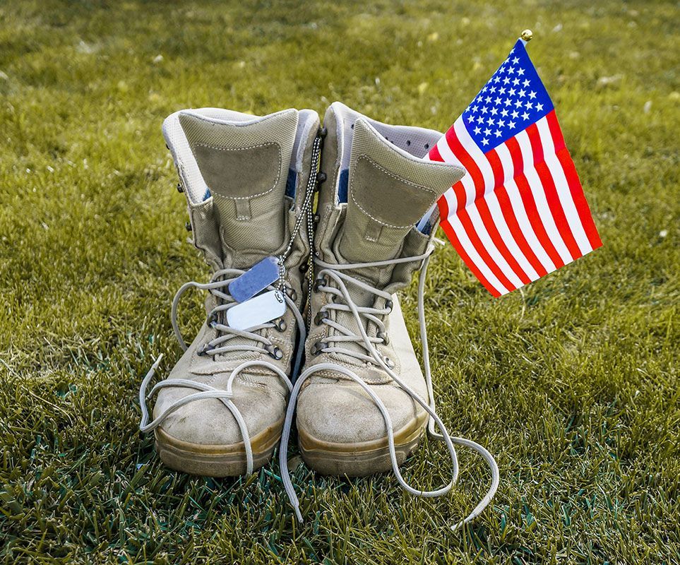 Worn military boots beside a small American flag on grass