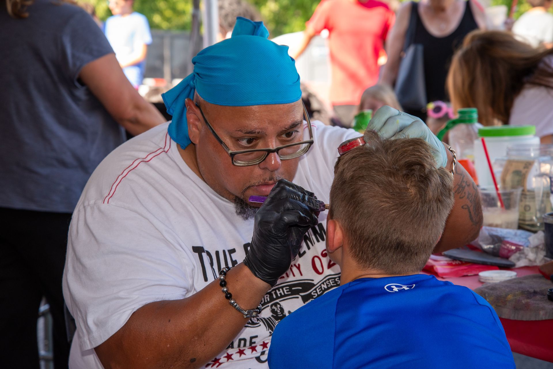 A man is painting a boy 's face at a festival.
