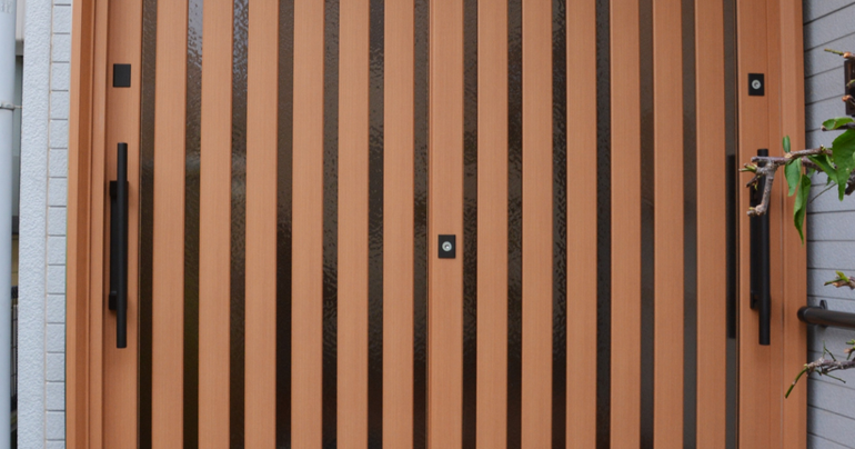 Light brown wooden double door with vertical slats, black hardware, and a center lock, set in a neutral-colored wall.