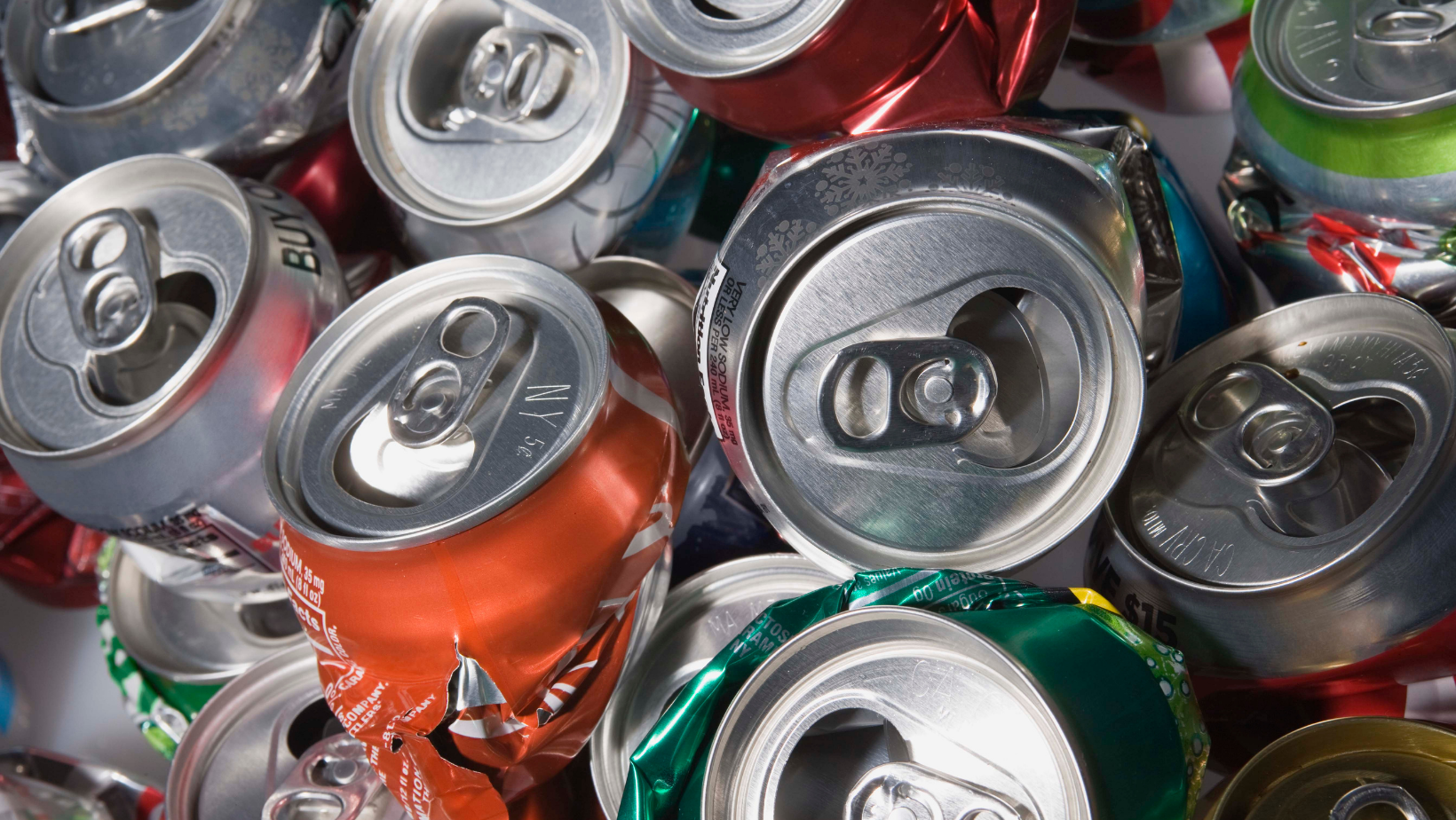 Crushed aluminum soda cans piled together, mostly silver with red and green labels