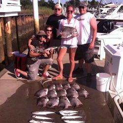 People posing on a dock beside a large catch of fish laid out on the ground.