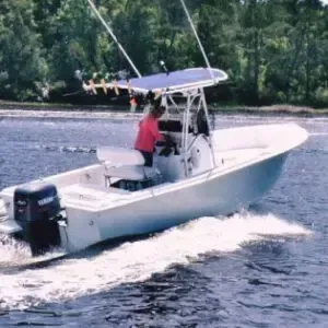 White center-console fishing boat speeding across water, with a person in a red shirt onboard.