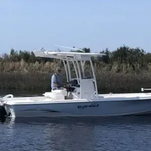 White center-console boat on calm water with one person aboard near marsh reeds