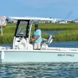 Man standing on a white Sea Pro boat on calm water beside grassy marshland