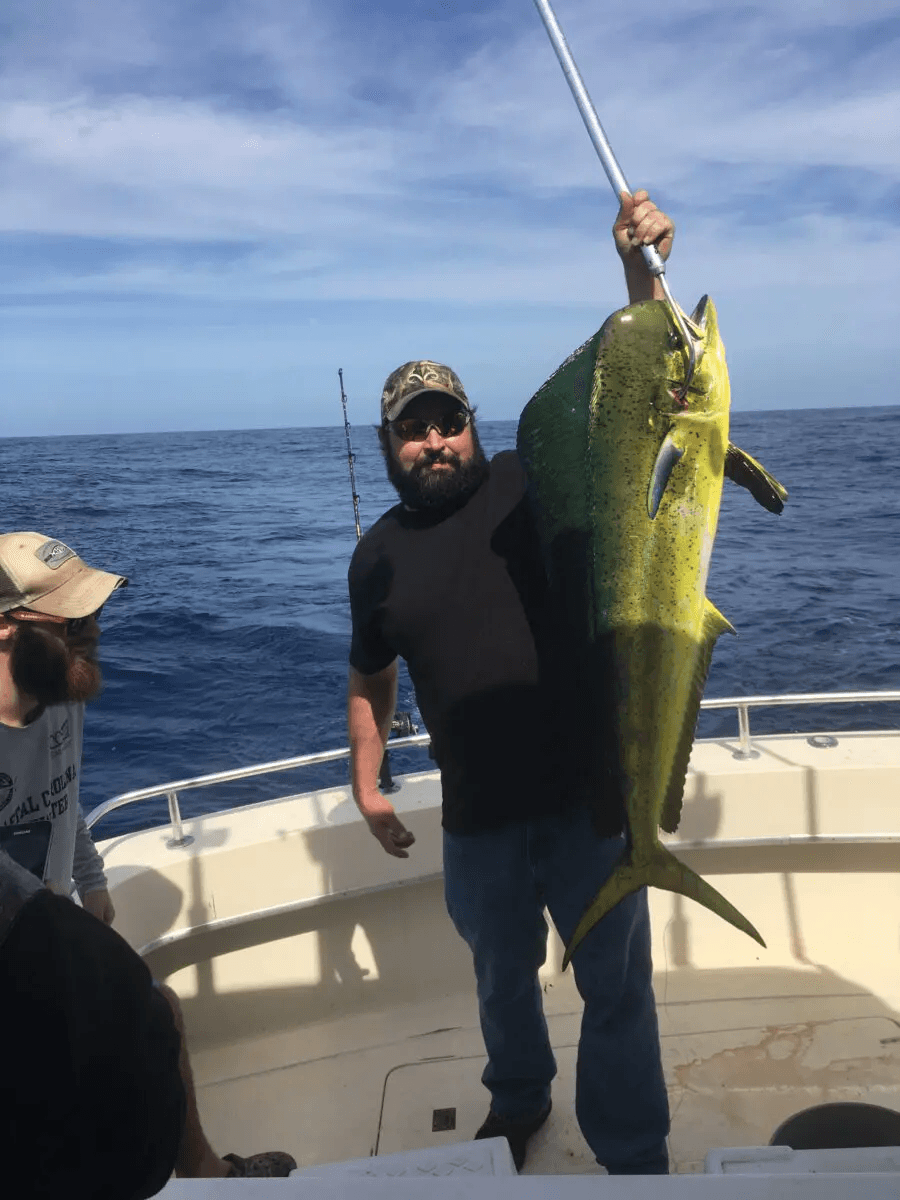 Man on a boat holding up a large yellow-green fish over the ocean