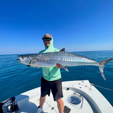 Angler on a boat holding a large fish over blue ocean under a clear sky