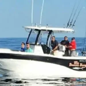 Four people on a white motorboat on open water under a clear blue sky.