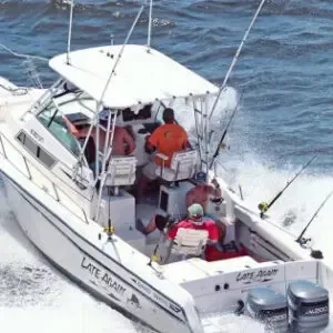 White sportfishing boat speeding through waves with three people on deck