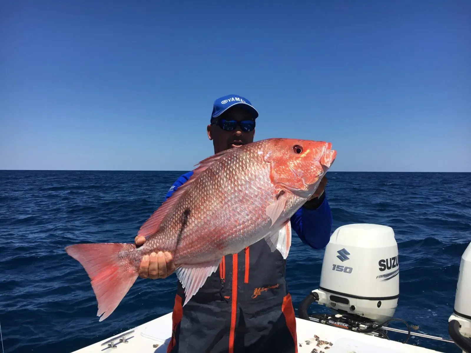 Person holding a large red fish on a boat at sea, with outboard motors visible.
