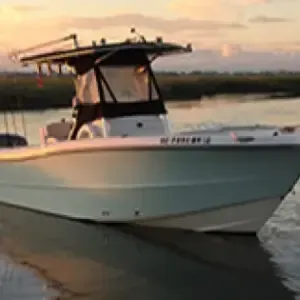 White motorboat on calm water at sunset, with a black canopy and soft orange sky.