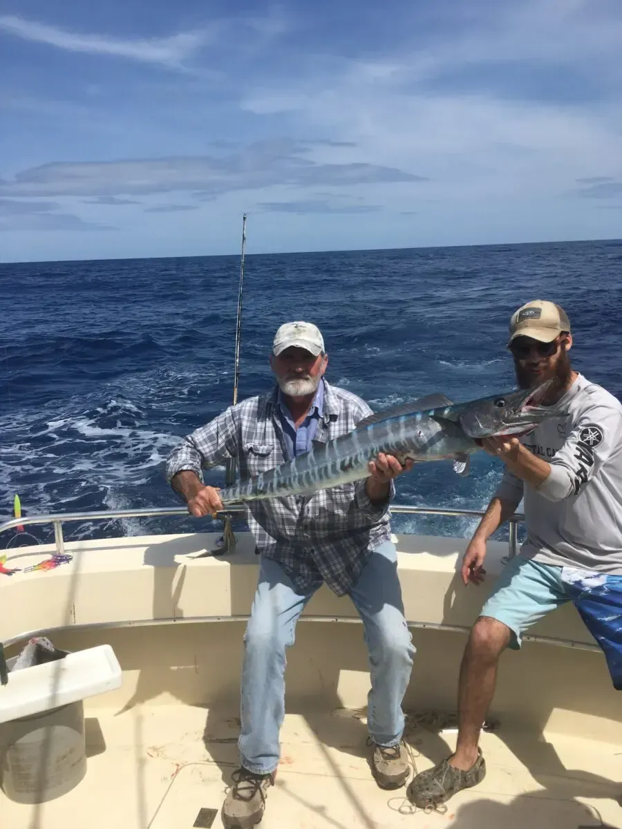Two men on a boat holding a large fish with the ocean behind them