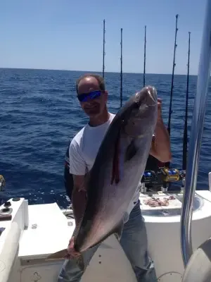 Man on a boat holding a large fish against a blue ocean backdrop