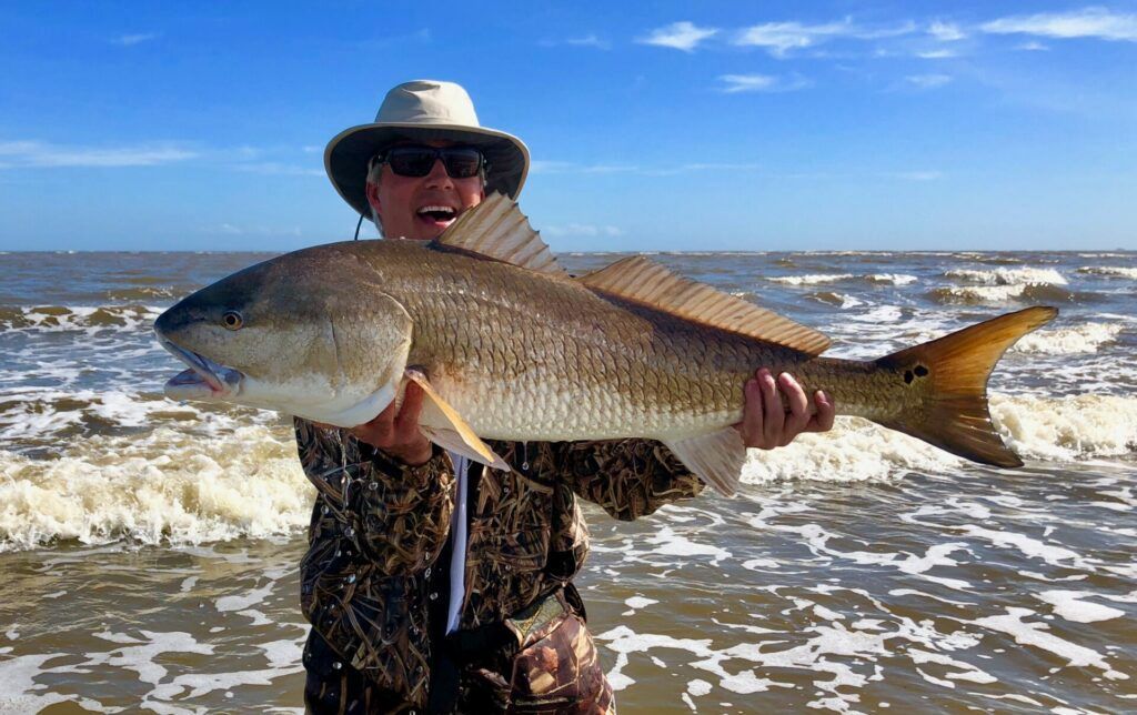 Person holding a large fish on a beach with waves in the background