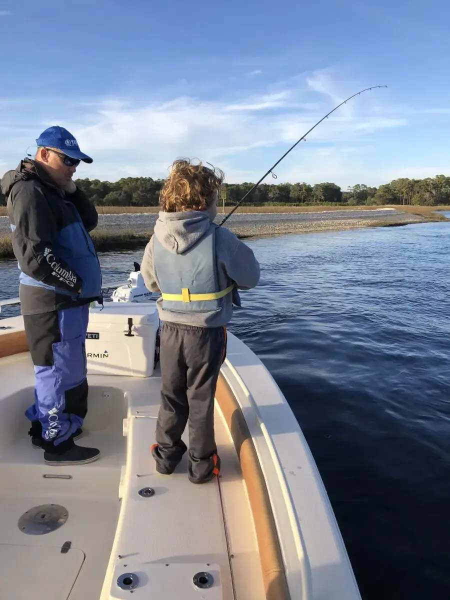 Two people fishing from a boat on calm water under a blue sky