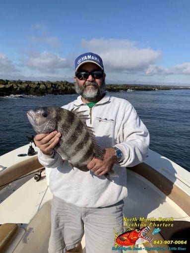 Man in sunglasses and cap holds a striped fish on a boat in sunny water