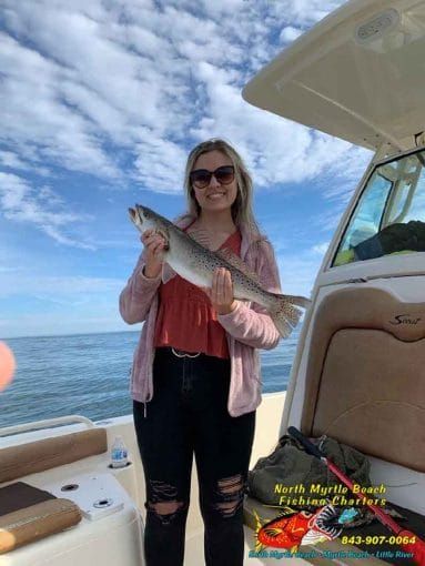 Woman on a boat holding a large fish beside the open cabin under a blue sky.