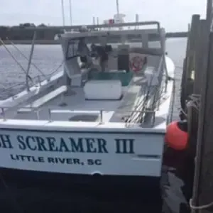 White boat docked at a marina, named “Fish Screamer III,” with fishing rods and calm water nearby