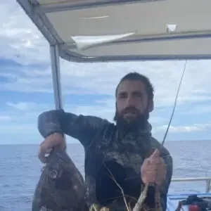 Man on a boat at sea holding up a large fish, with the ocean and sky behind him